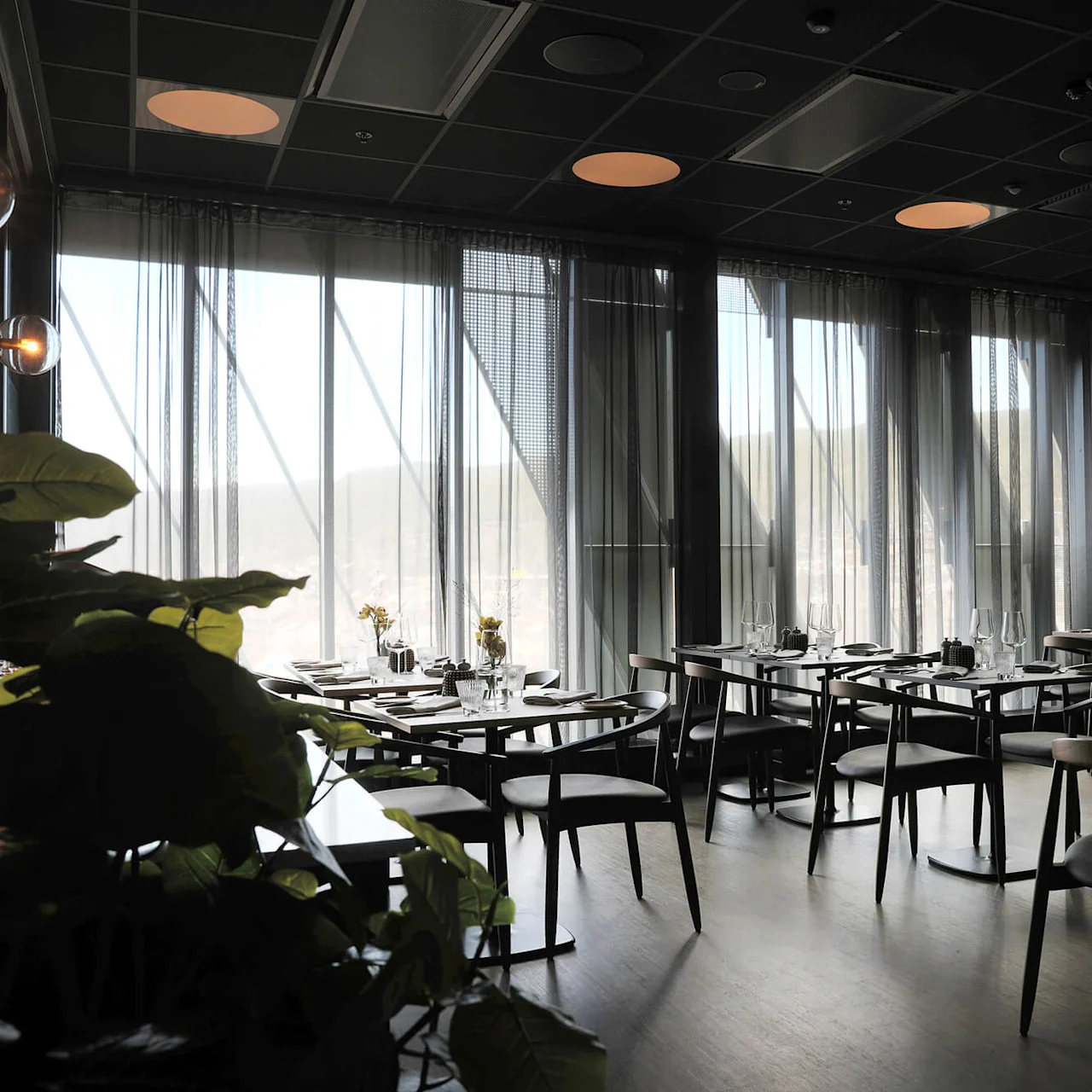 Elegant dining room with set tables, tall windows, and modern decor, radiating a sophisticated ambiance.