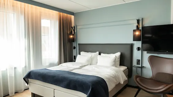 Et moderne og innbydende hotellrom med en komfortabel seng, en koselig lenestol og en flatskjerm-TV.