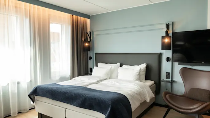 A modern and inviting hotel room with a comfortable bed, a cozy armchair, and a flat-screen TV.