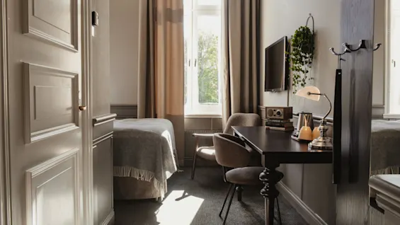 Ett varmt och inbjudande hotellrum badat i naturligt ljus, med en bekväm säng, en funktionell skrivbordsplats och fönsterutsikt.