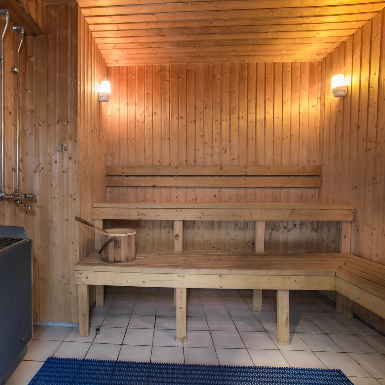 Ett träfodrad bastuinrede med bänkar och ugn, ingen synlig aktivitet, belyst för stämning.