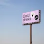 Mainostaulu, jossa lukee "Cold drinks", lasin kuvake ja nuoli, 500 metrin tauko, kirkasta taivasta vasten.