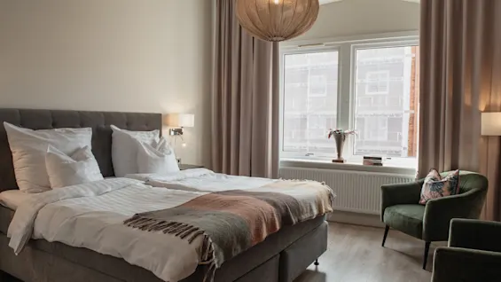 Et hyggeligt hotelværelse på Home Hotel Norre Park i Halmstad med en komfortabel seng, to grønne lænestole og et stort vindue.