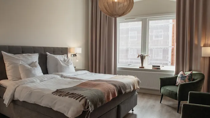 Et koselig hotellrom på Home Hotel Norre Park i Halmstad med en komfortabel seng, to grønne lenestoler og et stort vindu.