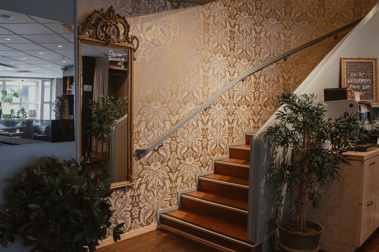 Utsmyckad trappa med guldmönstrad tapet, en stor spegel och växter. Texten lyder: Du ser fantastisk ut! Du ar valkommen Precis som ar.