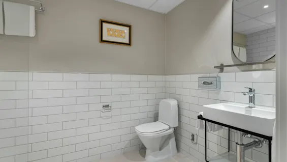 A clean and modern bathroom featuring white subway tiles, a toilet, a sink with a mirror, and fresh towels.
