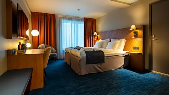 Ett välupplyst hotellrum med en stor säng, möblering och varma färgaccent.