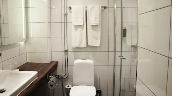A modern bathroom with white tiles, featuring a toilet, sink, and shower with glass door.