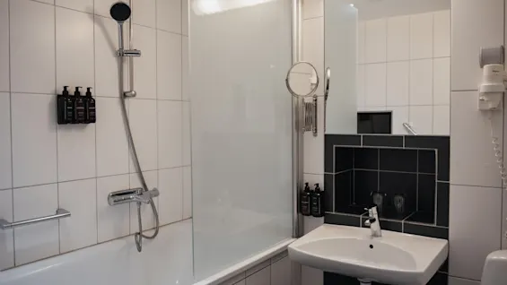 Ett rent och modernt hotellbadrum med badkar, dusch, handfat och spegel, redo för en uppfriskande upplevelse.