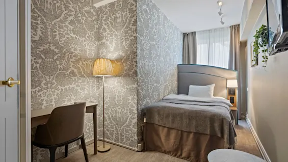 A welcoming hotel room featuring a comfortable bed, a functional desk area, and soft lighting, with decorative wallpaper.