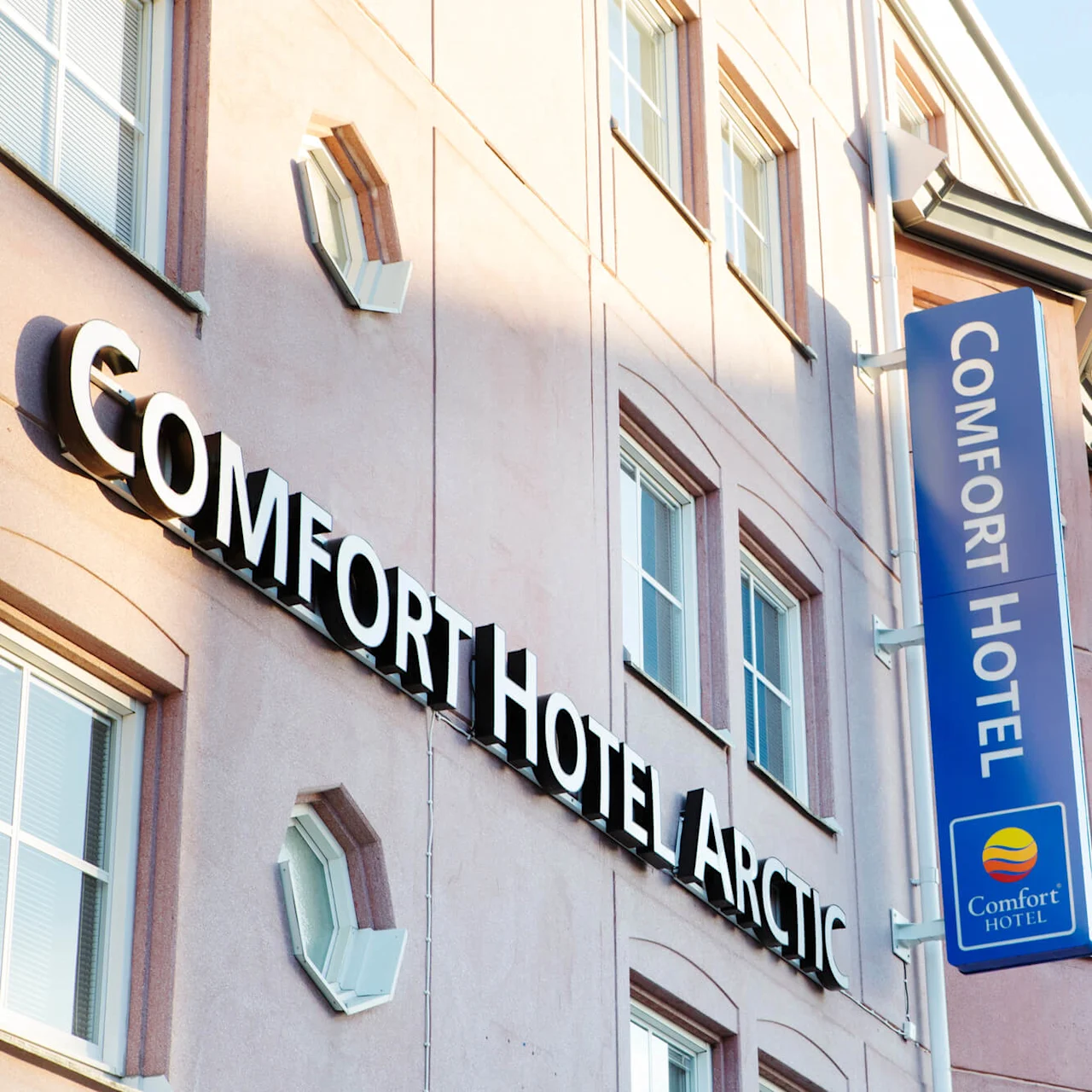 A hotel sign reading "COMFORT HOTEL ARCTIC" attached to a building's facade against a clear sky.