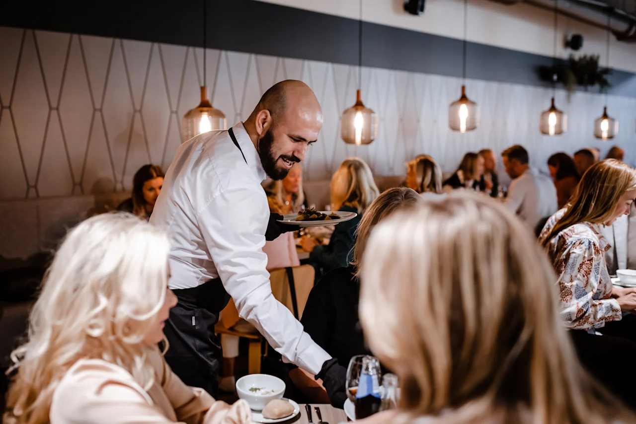 En servitør serverer et måltid til gjester på en livlig restaurant på Quality Hotel Arlanda XPO.