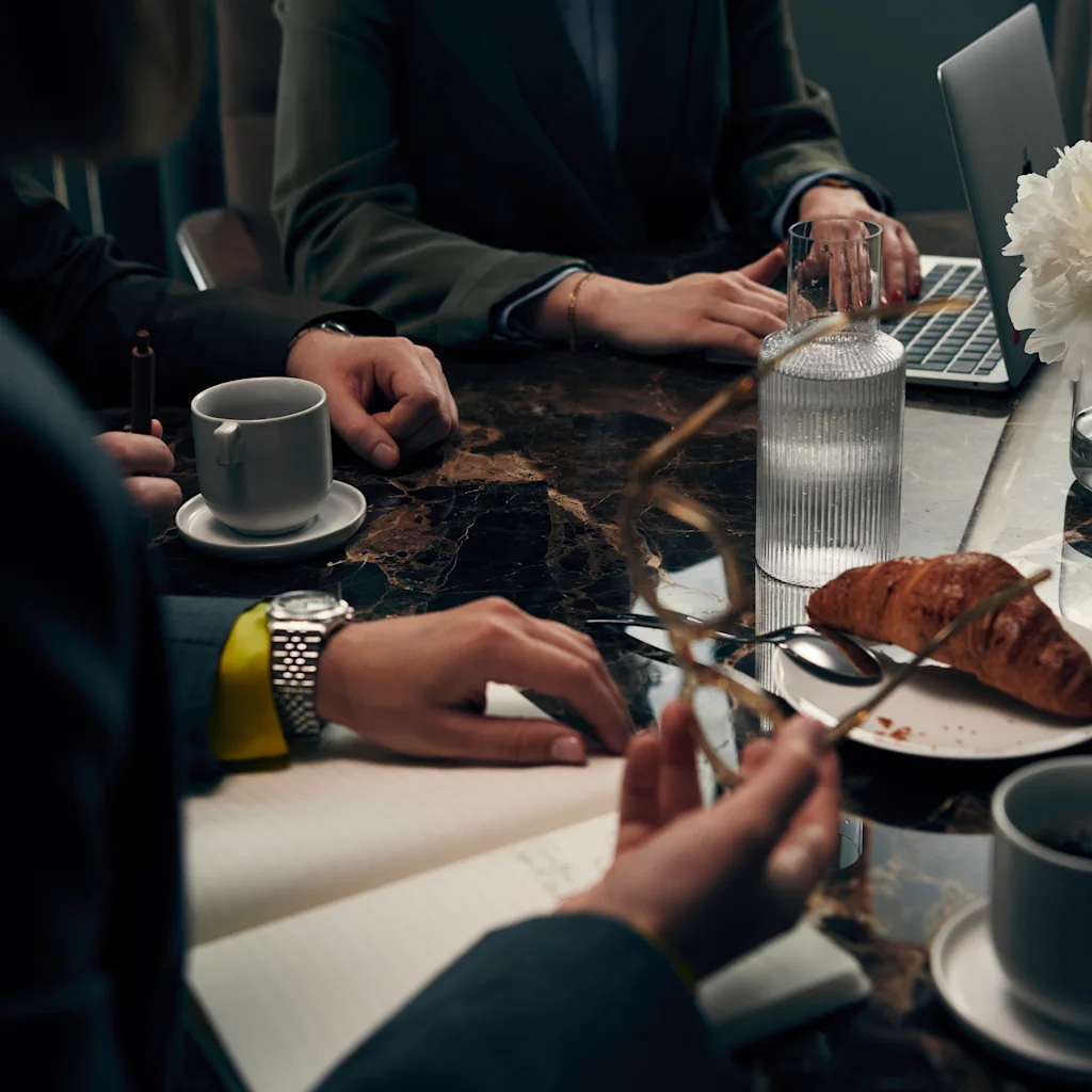 Folk der arbejder eller mødes ved et bord med kaffe, en croissant og en bærbar computer.