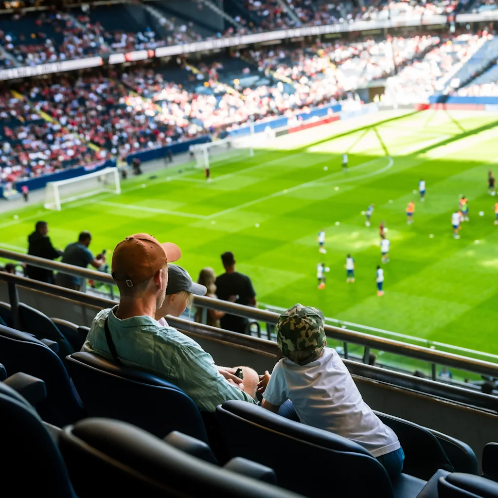 Katsojat stadionilla katsomassa jalkapallo-ottelua aurinkoisena päivänä.