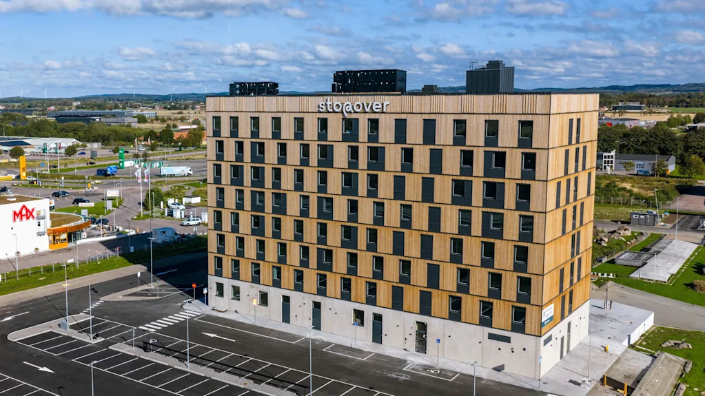 En rektangulär byggnad med flera våningar märkt "Söderöver" står mot en bakgrund av ett förortsområde. I närheten syns en "Max"-snabbmatsrestaurang längs ett gatunät.