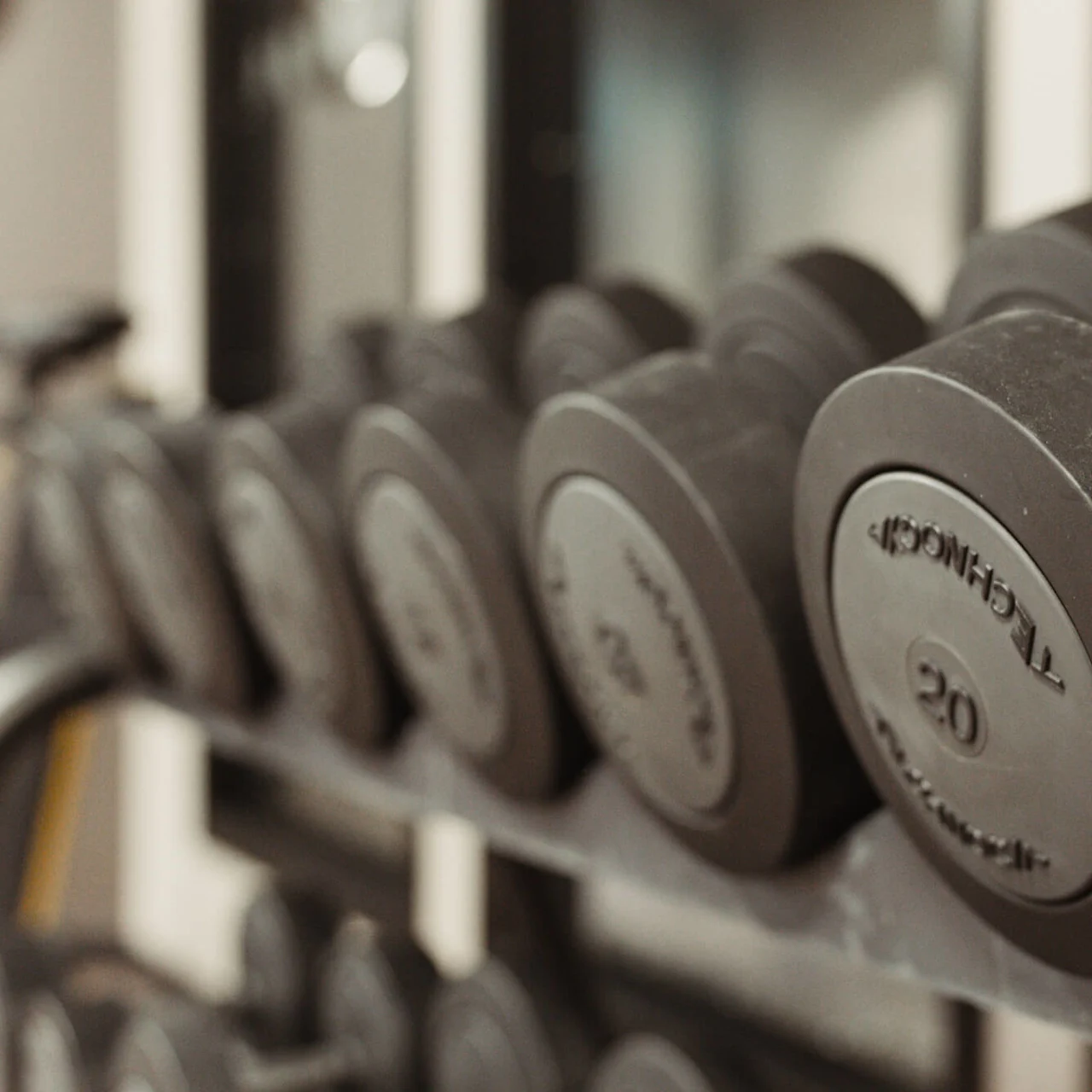 Håndvægte ligger på et metalstativ, hver mærket "IRONCO." og "20." Vægtene er pænt arrangeret i et fitnesscenter.