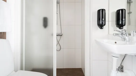 Et lyst og funksjonelt baderom med toalett, et flislagt dusjområde og en vask utstyrt med såpedispensere.