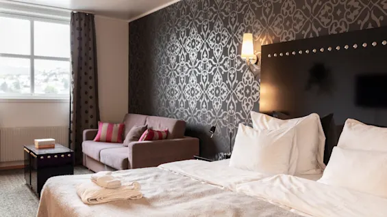 Mukava ja kutsuva hotellihuone, jossa on suuri sänky, viihtyisä sohva ja tyylikäs kuviollinen tapetti.