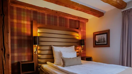 A cozy bedroom with a neatly made bed, soft lighting, and wooden beams, suggesting a comfortable, inviting atmosphere.
