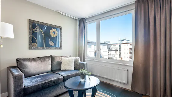 A velvet sofa and abstract painting in a modern living room with natural light from a large window.