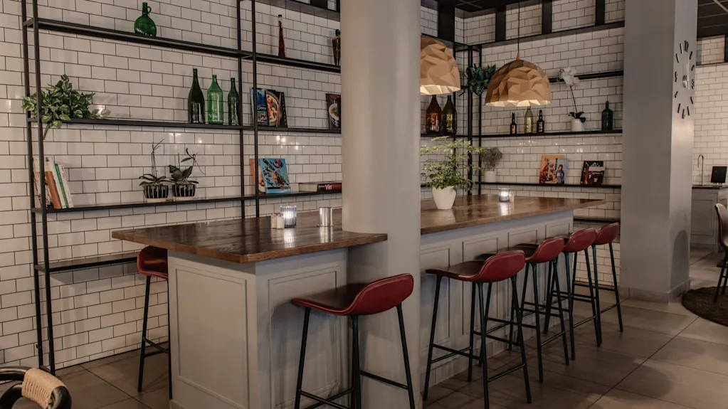 Tyylikäs baarialue, jossa on pitkä tiski, punaiset tuolit ja koriste-esineillä koristellut hyllyt.
