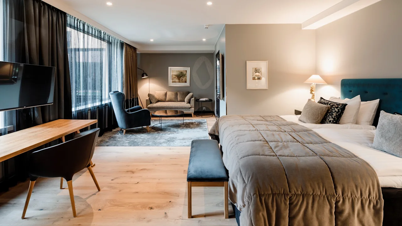 Tilava ja kutsuva hotellihuone, jossa on suuri sänky, viihtyisä oleskelutila ja toimiva työpiste.