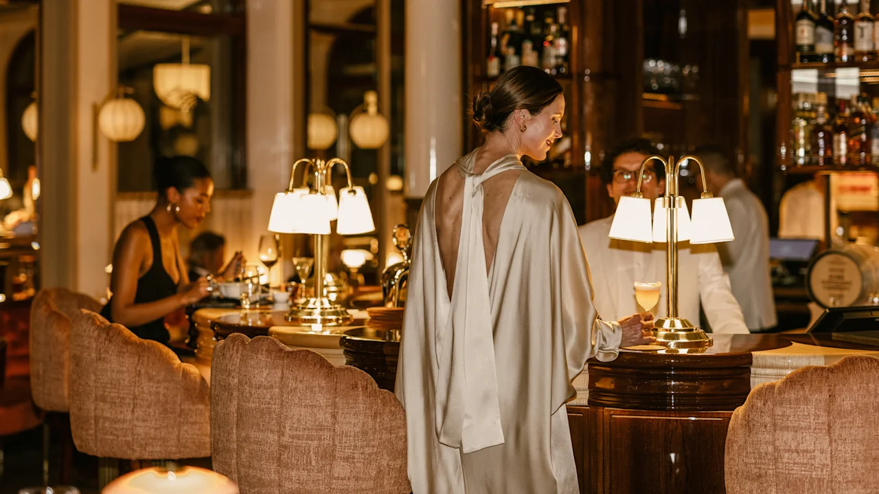 Guests enjoying an evening out, with some at the bar and others dining in a warm, inviting atmosphere. Hotel Kämp – Kämp Bar.