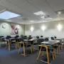 Et ryddig konferanserom med tomme stoler og bord venter på deltakere. En klokke og veggkunst gir karakter, mens papirer er pent plassert på skrivebordene og skaper en profesjonell, men innbydende atmosfære.