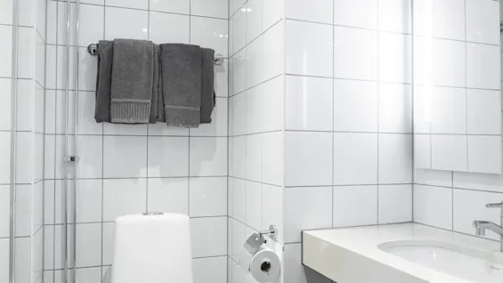 Hyvin hoidettu kylpyhuone, jossa on valkoiset laatat, wc, pesuallas ja puhtaat pyyhkeet, tarjoten puhtaan ja kutsuvan tilan.