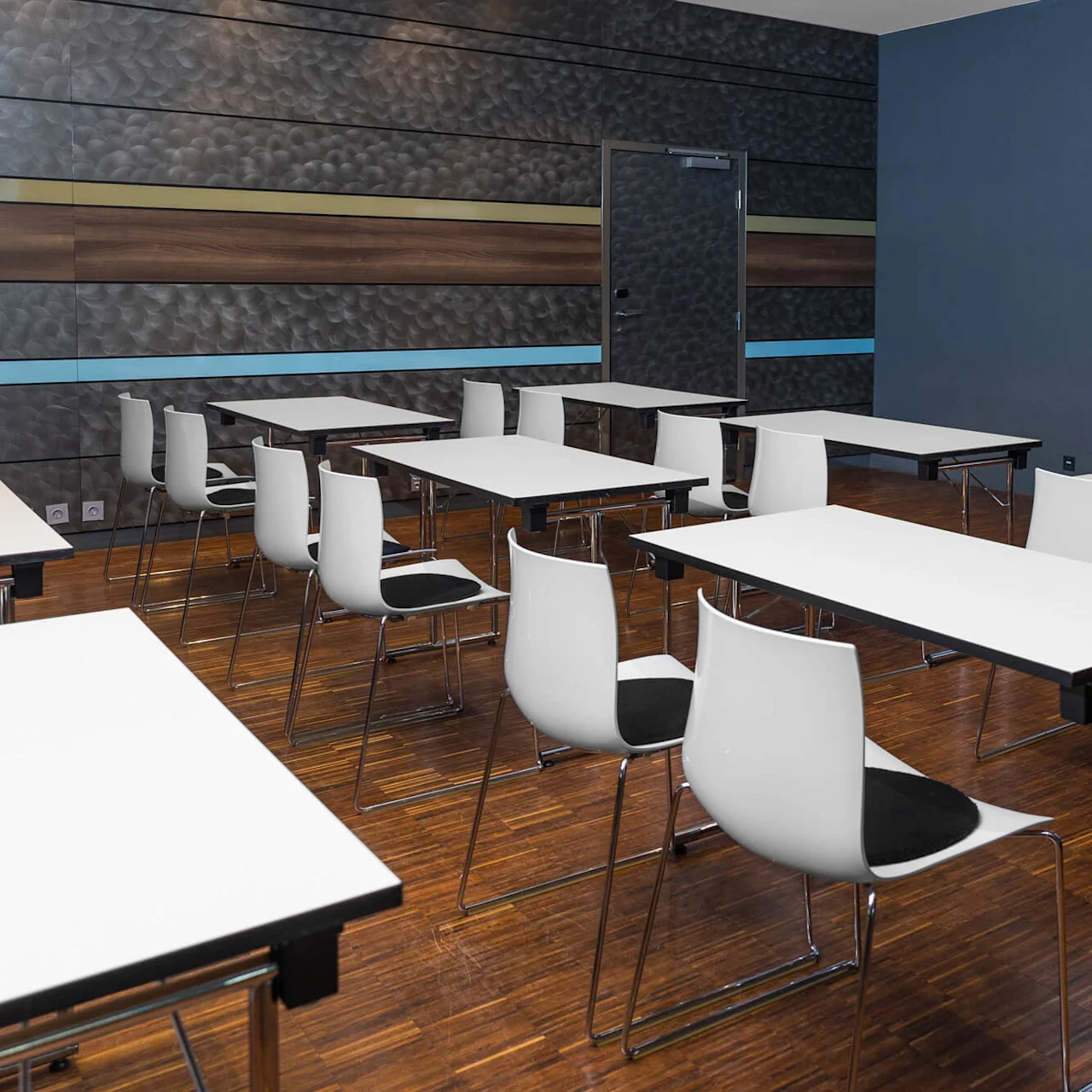 Desks and chairs are arranged in neat rows in a conference room. A large screen on the wall displays the text "Comfort Hotel". The room has a modern design.