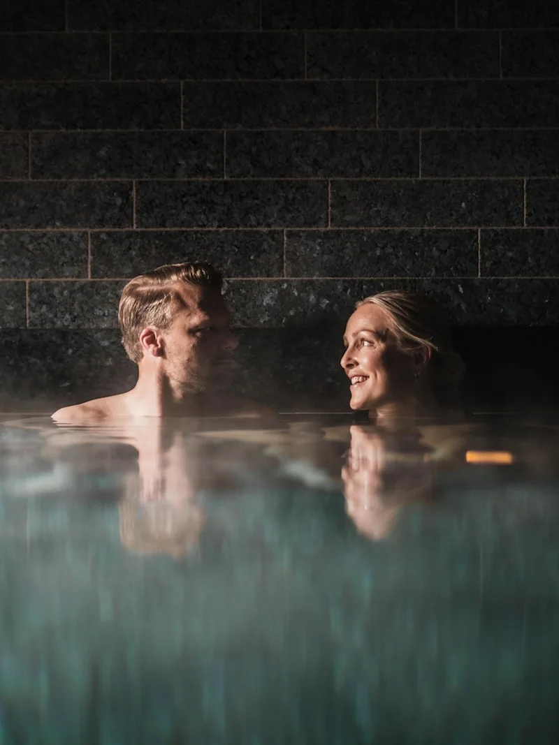 Two people enjoying a relaxing moment in a steamy pool at Farris Bad in Larvik, smiling at each other.
