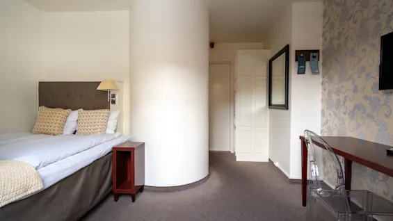 Et koselig hotellrom med seng, skrivebord og en unik sylindrisk søyle, som tilbyr et komfortabelt opphold.