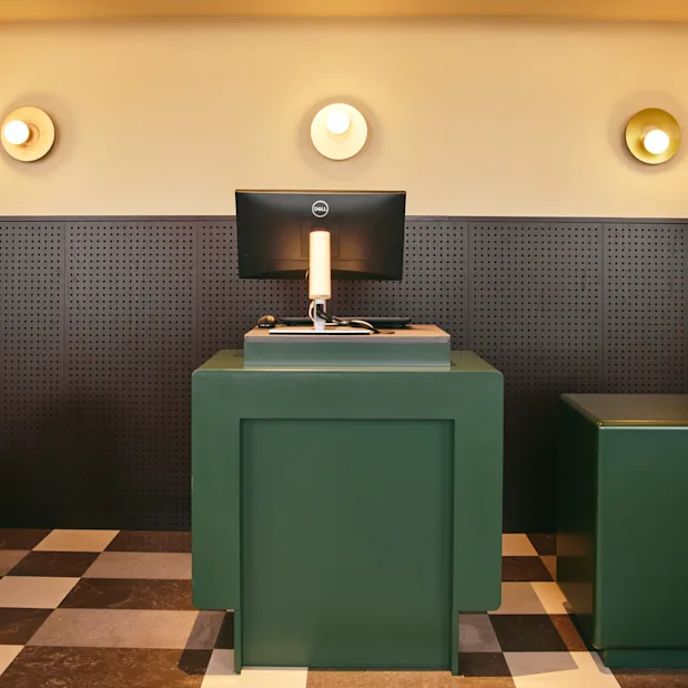Det innbydende resepsjonsområdet på Stopover Hotel Falkenberg, med stilige grønne disker, en datamaskin og et særegent rutete gulv.