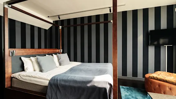 Et stilfuldt hotelværelse med en himmelseng, blåt sengetøj, stribede vægge og et fjernsyn.