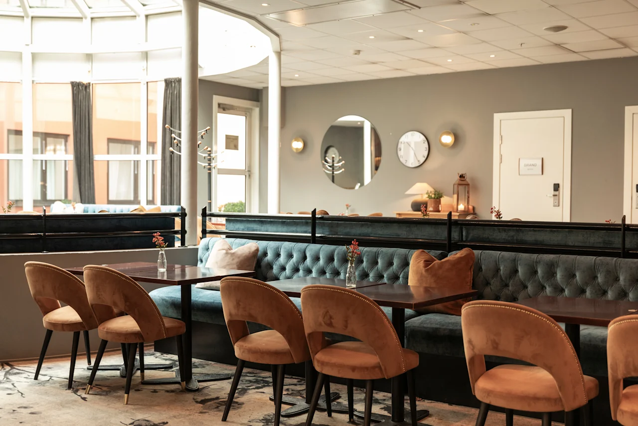 Inviting dining area at Home Hotel Grand Bodø with comfortable seating, tables, and natural light. A sign on the door reads GRAND.