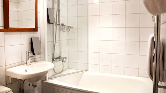A bathroom interior with a shower over a bathtub, sink, mirror, and white tiled walls.