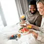 A smiling couple enjoying breakfast in bed in a hotel room.