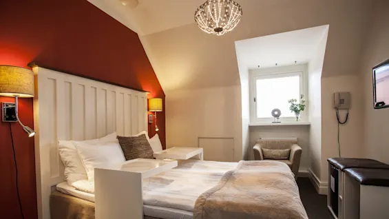 Et koselig hotellrom med oppredd seng, varmt lys, og sitteområde, som antyder komfort og hvile.