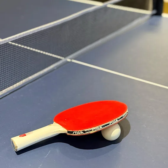 Et rødt bordtennisbat der hviler på en hvid bold oven på et blåt bordtennisbord.