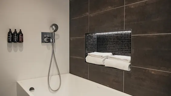 Et rent og moderne hotelbadeværelse med badekar, bruser og friske håndklæder på en forsænket hylde. tilføj Home Hotel Norre Park i Halmstad.