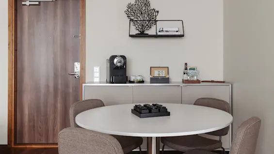 Ett mysigt hotellrum med ett runt matbord och stolar, en kaffestation och en dekorativ hylla.