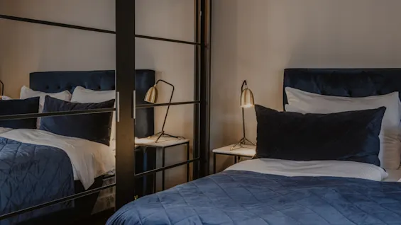 Ett mysigt sovrum på Home Hotel Grand, Helsingborg, med en säng med blå sängkläder och en varm sänglampa.