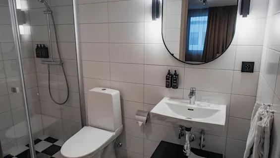 Ett rent, modernt badrum med dusch, toalett och handfat. Svartvita rutiga golvplattor ger en stilfull känsla.