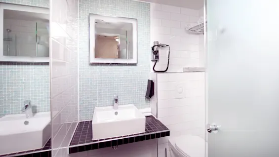 A modern bathroom with a rectangular sink, mirror, and shower reflected in the glass door.