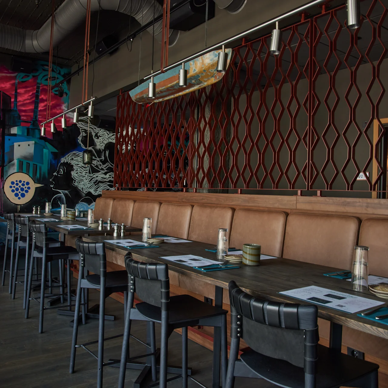 En rad med tomma matbord med stolar längs en läderbänk. Färgglada väggmålningar och modern inredning skapar en konstnärlig restaurangatmosfär.