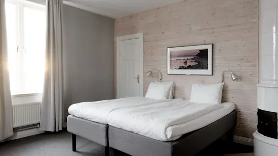 Ett mysigt hotellrum med två sängar, ett fönster med starkt ljus och en dekorativ öppen spis.