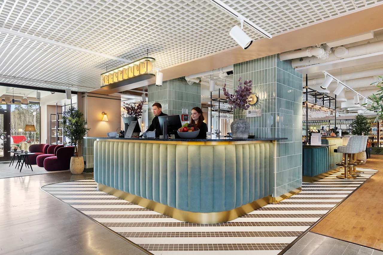 To ansatte som står bak en moderne hotellresepsjon og ønsker gjester velkommen.