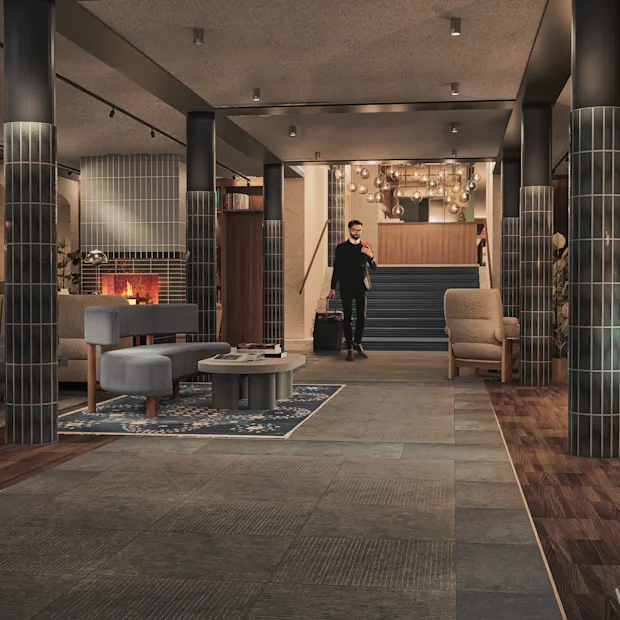 Hotel lobby with a guest arriving, a reception desk, and a cozy lounge area with a fireplace. 