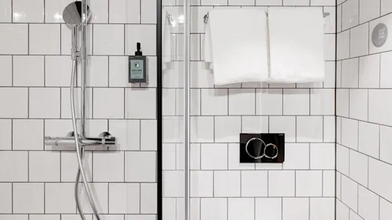 A sleek chrome shower against a tiled wall features a showerhead, soap dispenser labeled "Hair & Body," and white towels on a rack. Text reads, "GO EASY ON THE PLANET."