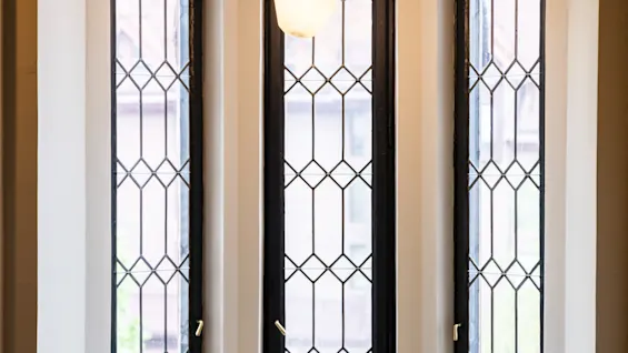 Mysigt fönsternisch med en vadderad bänk prydd med fyra kuddar, belägen under tre höga, smala fönster med diamantmönstrat glas. En hängande belysning lyser upp platsen.